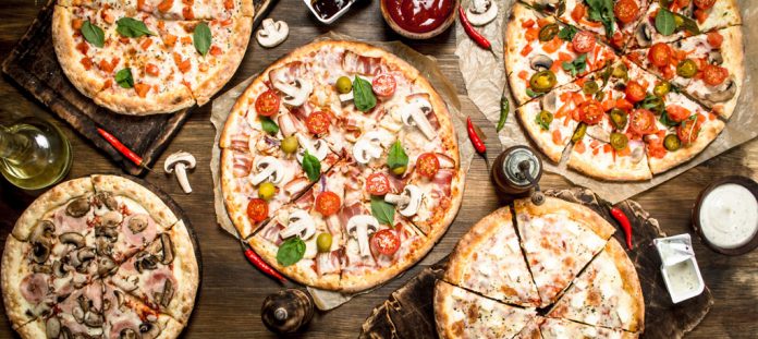pizzaweb A variety of pizzas on a table as seen from above.