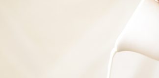 A glas of Iced Coffee with Milk being poured into it from a white pitcher.