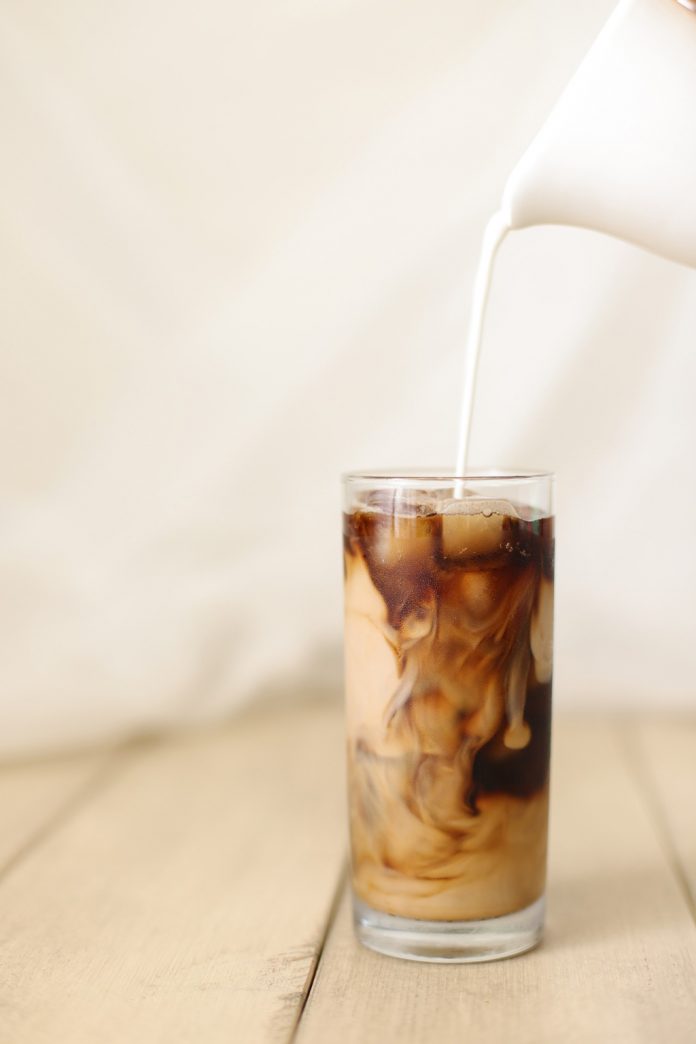 Iced Coffee A glas of Iced Coffee with Milk being poured into it from a white pitcher.