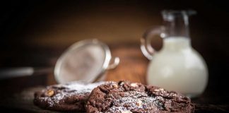 Cocoa Chocolate Chip Cookies with a pitcher of milk and a sifter in the background.
