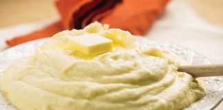 A serving bowl of Cheesy Maple Mashed Potatoes with a pat of butter on top.