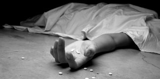 A black and white image of an addict, dead beneath a sheet, arm outstretched, pills in the palm of their lifeless hand and littering the floor near their hand.