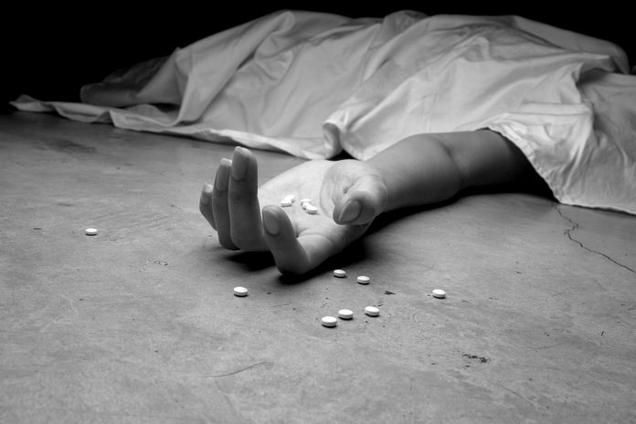 Death of an Opioid Addict A black and white image of an addict, dead beneath a sheet, arm outstretched, pills in the palm of their lifeless hand and littering the floor near their hand.