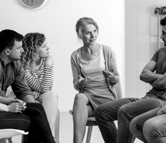 A diverse group of people sit and talk during a group counseling session.