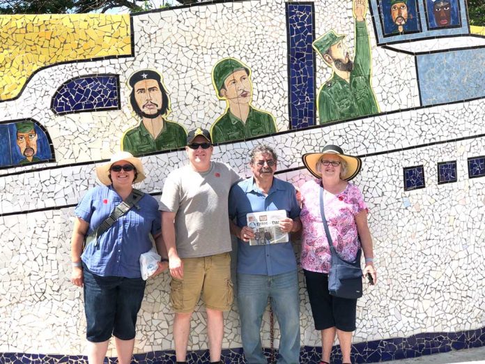 Joyce and John Paglialunga and their children, John and Jeana, stand in front of a mosaic wall depicting Fidel Castro and Guerrillero Heroico.