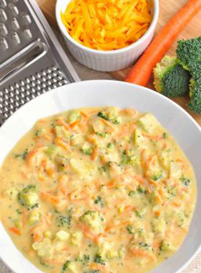 A bowl of broccoli cheddar soup A bowl of broccoli cheddar soup with cheese, carrots, broccoli and a grater in the background