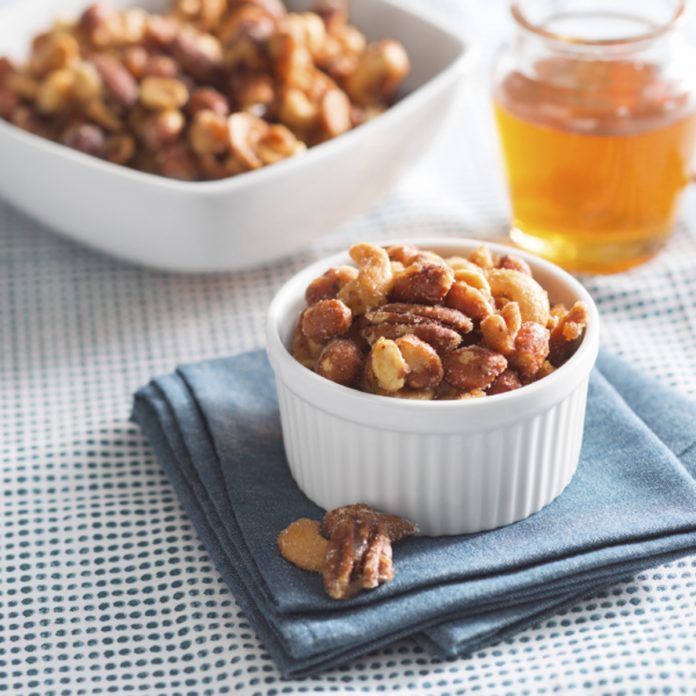 Honey Roasted Bridge Mix A small bowl of Honey roasted bridge mix, sits on top of a blue napkin with a larger bowl of the mix and a glass jar of hone in the background.