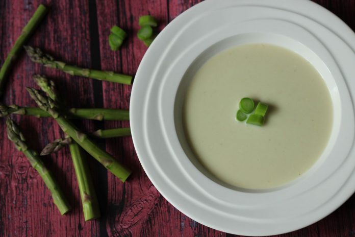 asparagus-soup A bowl of light green soup with slices of asparagus in the center and shots on the table beside the bowl