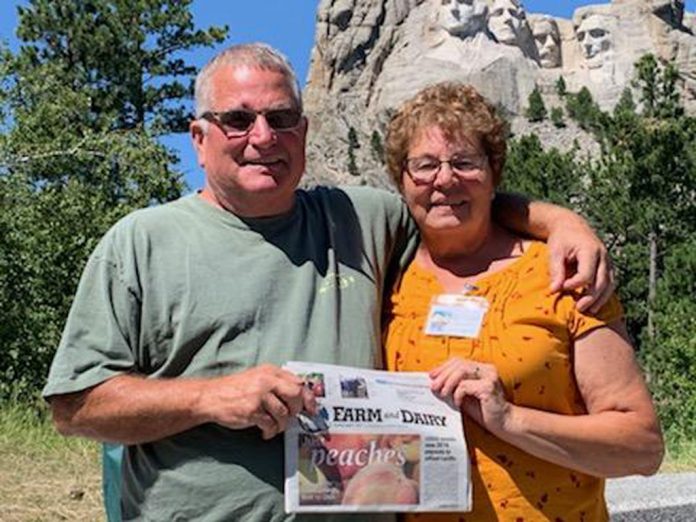 vac-burrier Tom White and Elizabeth Burrier stand in front of Mt. Rushmore with their Farm and Dairy newspaper in hand.