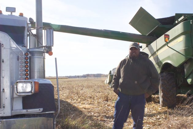 A farmer stands between a semi truck and a combine.