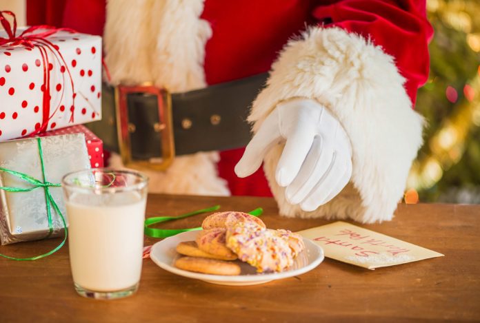 feature.web Santa reaching for cookies on a plate with a glass of milk nearby
