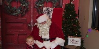 A child sits on a yellow toy tractor in front of Santa.