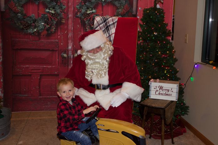 santa_on_the_dairy_farm_9 A child sits on a yellow toy tractor in front of Santa.