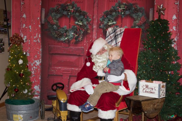 A two-year-old blonde boy sits on Santa's lap.