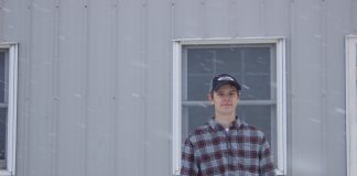 Michael Baer, 18, stands in front of a barn at Rogers Community Auction while it snows.