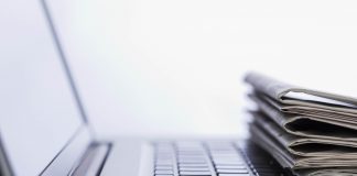 A computer with papers stacked on the keyboard.