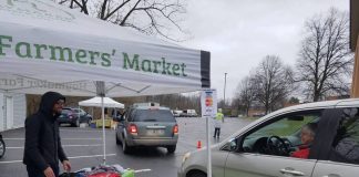 A man stands under a tent at a farmers market and talks to a woman in her car.