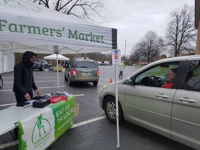 covid19_farmers_markets_1 A man stands under a tent at a farmers market and talks to a woman in her car.