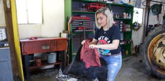 A woman pulls a cover off of a tractor engine.