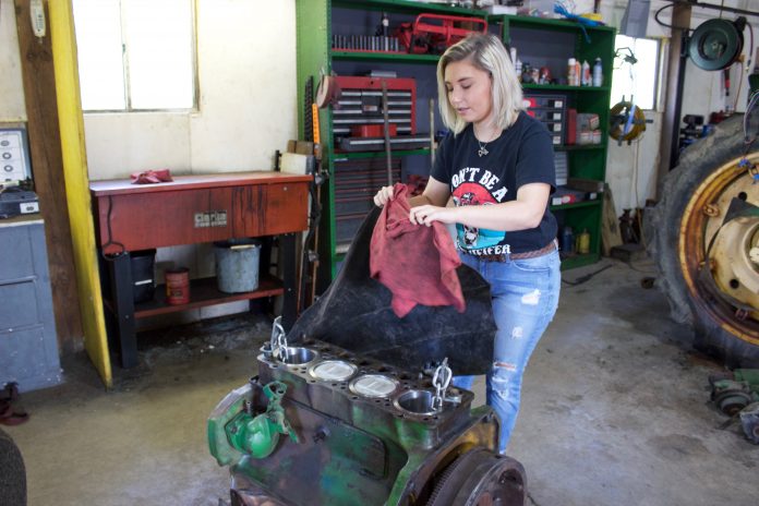 benton_family_1 A woman pulls a cover off of a tractor engine.