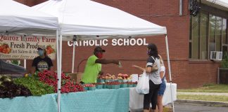 A man serves a woman from behind his stand at a farmers market.