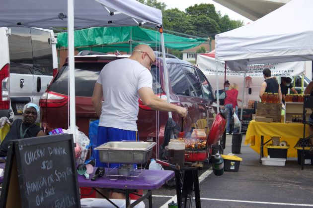 A man cooks on a grill at a farmers market.
