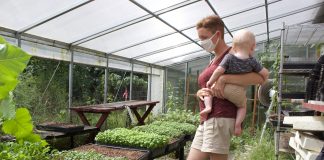 A woman stands in a greenhouse holding a baby.