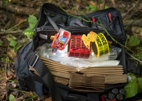 A bag filled with crime scene tape sits on the ground in the woods.
