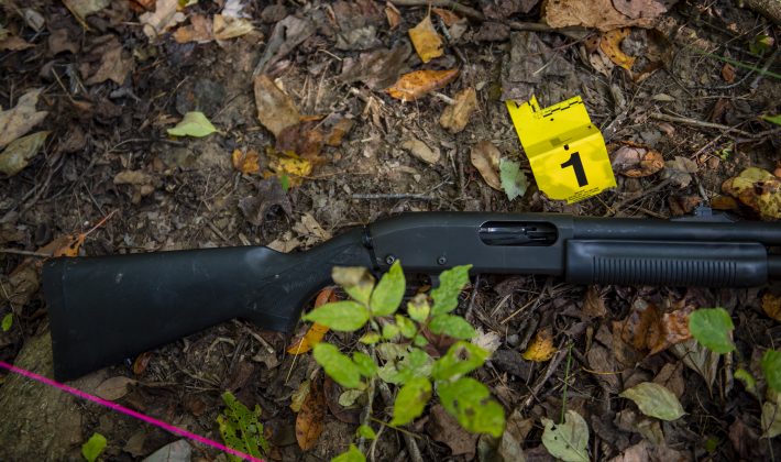 A shotgun lies on the ground with an evidence tag next to it.