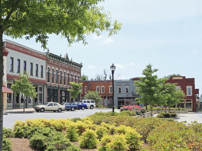 small town metro A small town with cars parked outside the buildings and trees and other greenery in front of it.
