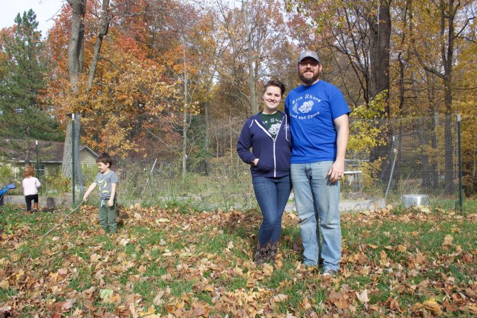 erie_shore_8 A woman and a man stand in front of a garden in the fall while a girl and a boy play in the background.