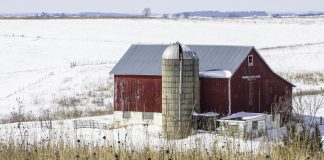 A barn and silo in the winter, with snow on the ground.