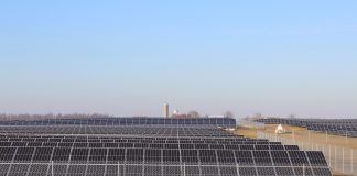 solar panels sit in a field with a barn and silo in the background