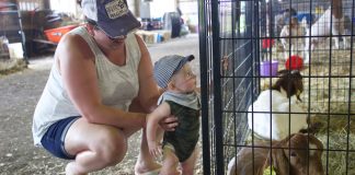 A woman and a child stand next to a goat pen at the fair.