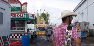 A 4-H'er shows off pins on his fair king sash on the midway at a fair.