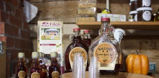 Bottles of maple syrup and small glasses set up for sampling on a table in a store.