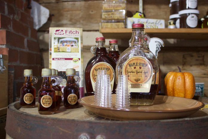 fitch_pharm_farm_4 Bottles of maple syrup and small glasses set up for sampling on a table in a store.