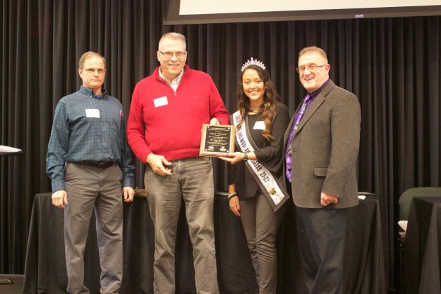 Three men and one woman stand on stage with an award.