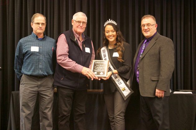 Three men and a woman stand on stage with an award.