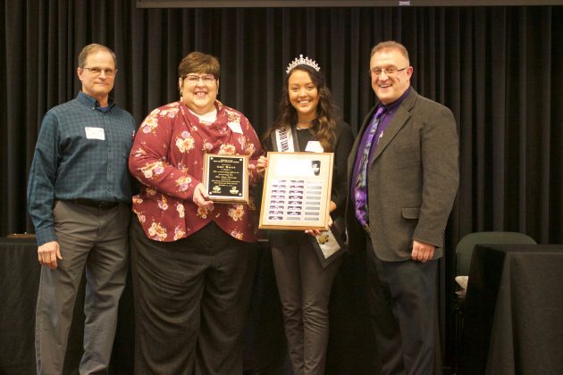Two men and two women stand on stage with an award.