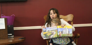 a woman reads a book to a group of people with a daughter on her lap