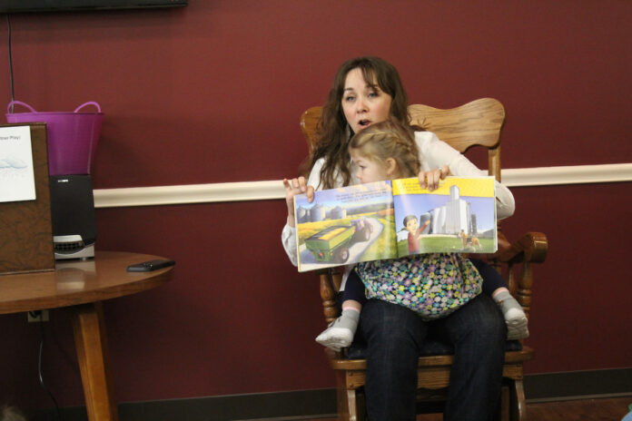 ag-literacy-day copy a woman reads a book to a group of people with a daughter on her lap