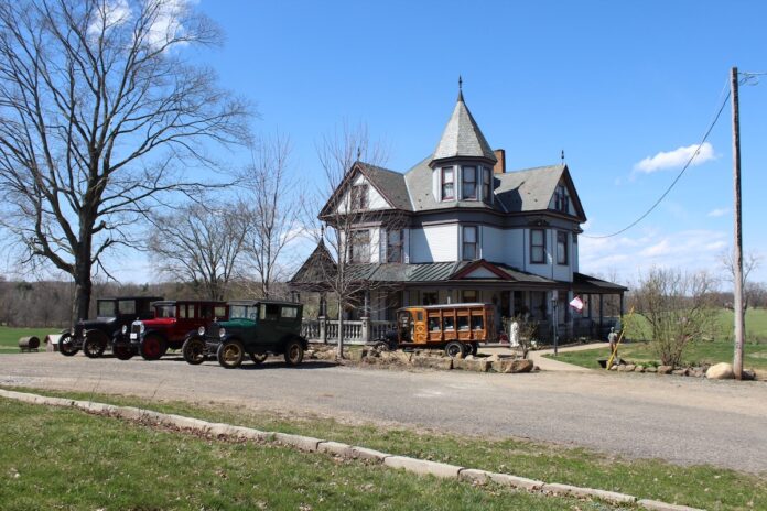 jim-hawk-1 copy antique cars sit outside a victorian home. A home built hearse sits in front of the home with a casket in the back.