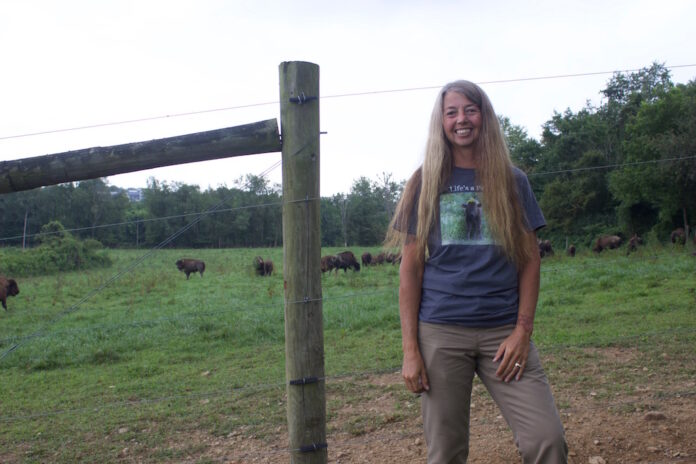 bison_ranch_1 A woman stands in front of a fence, with bison on the other side.