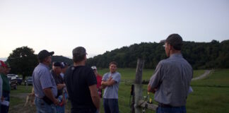 A group of farmers stand near a fence at a beef cattle farm.