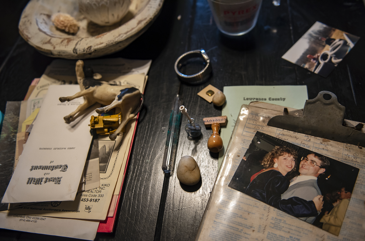 Items sit on a table, including a photo of a couple smiling, a toy cow, a stamp and other various trinkets.