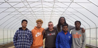 Five students and a teacher stand in a high tunnel