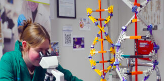high school student looks through microscope with helix models on table