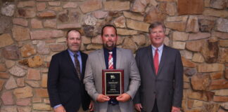 three men stand together while the one standing in the middle holds a plaque