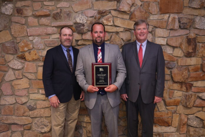 ty etgen three men stand together while the one standing in the middle holds a plaque